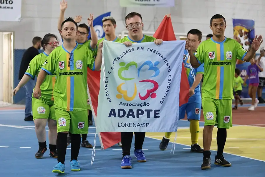 Atletas da ADAPTE entrando em uma competição com a bandeira da instituição